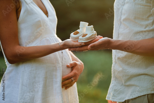 Pregnant woman with her husband holding child shoes. Pregnancy, maternity, preparation and expectation concept. Close-up, copy space, indoors. Beautiful tender mood photo of pregnancy.