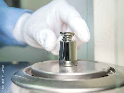фотографія A operator's hand is holding steel calibration weight to place on the analytical balance