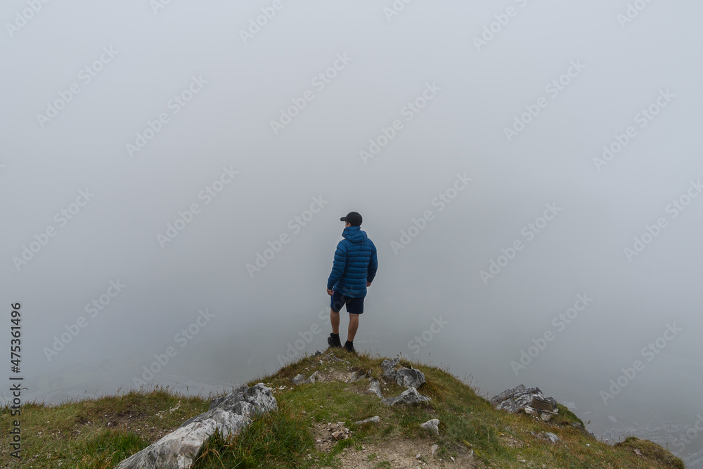 Obraz premium Man standing on top of mountain admiring landscape with fog