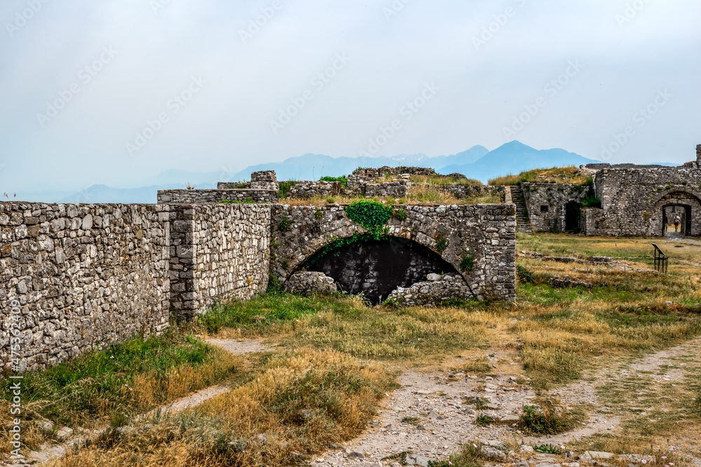 Ruins of ancient stone buildings in Shkoder Castle, Albania. Medieval stone walls among a yellow-green summer lawn in Rozafa fortress