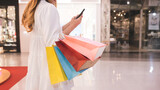 girl holding colorful shopping bags While walking in a shopping mall, a young woman uses her smartphone to find fashion stores in the mall.