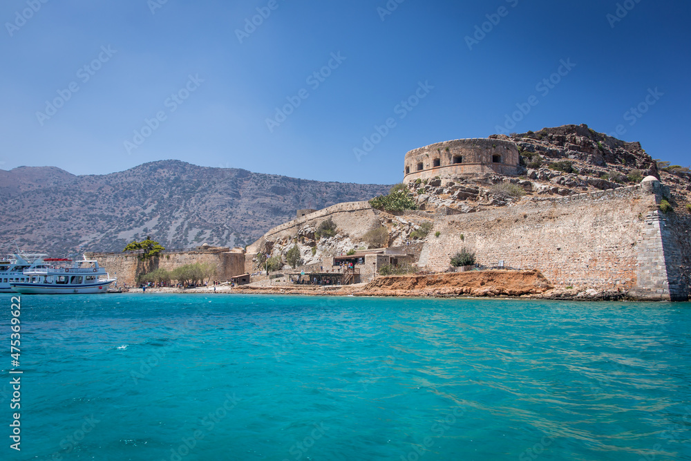The beautiful island and fortress of Spinalonga or Kalydon surrounded by turquoise colored Mediterranea Sea and mountains, visiting by tourists and Greek boats. The beautiful island and fortress of Spinalonga or Kalydon surrounded by turquoise colored Mediterranea Sea and mountains, visiting by tourists and Greek boats.