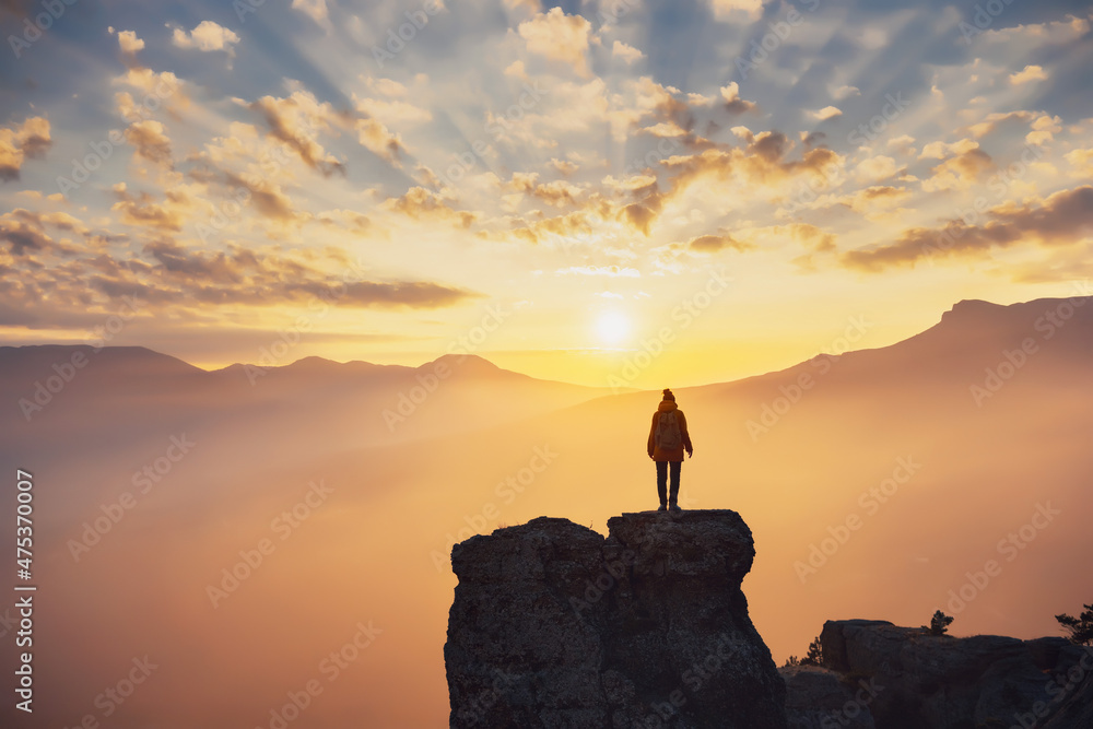 Silhouette of hiker girl enjoying sunlight in mountains at sunset
