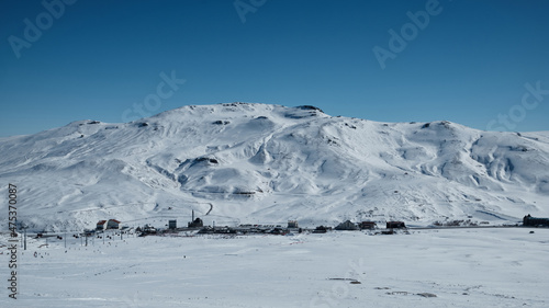 Snow covered mountain slope with clouds and bright blue sky. Winter snowy bright morning mountain landscape