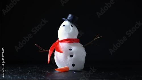 Funny snowman in stylish hat and red scalf melting on black background. Studio timelapse video. UHD 4K time lapse
