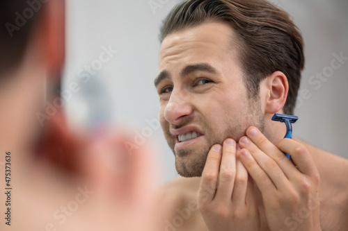 Fotografija Young man shaving and looking disturbed