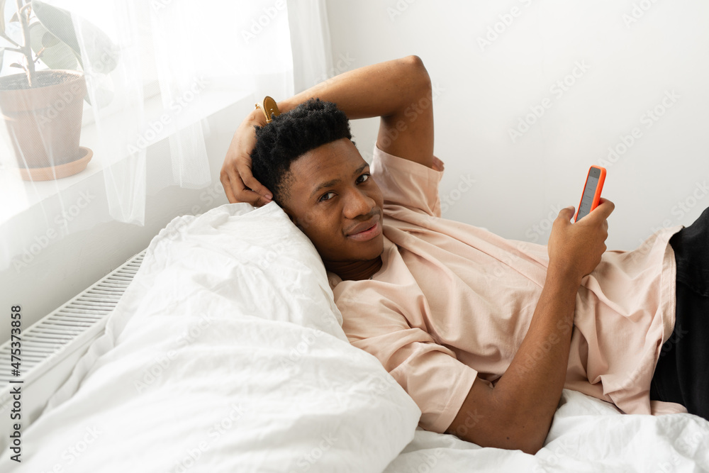 african young man lying on bed with mobile phone african young man lying on bed with mobile phone