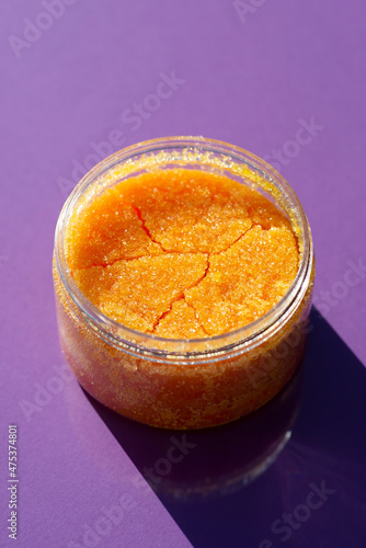 Open jar with orange sugar body scrub texture on a purple background. Skincare products , natural cosmetic. Beauty concept for body care