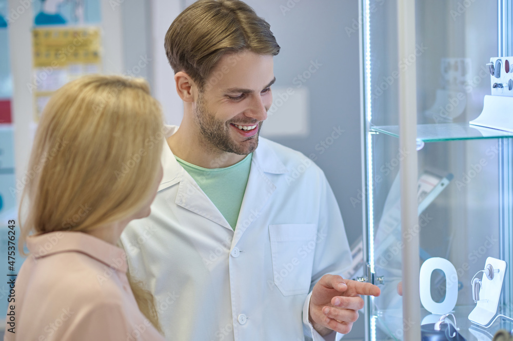 Man in white coat pointing at hearing aid and woman Man in white coat pointing at hearing aid and woman