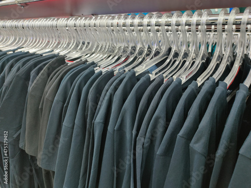 a row of plastic transparent hangers with dark monochrome t-shirts on a shiny metal rack 