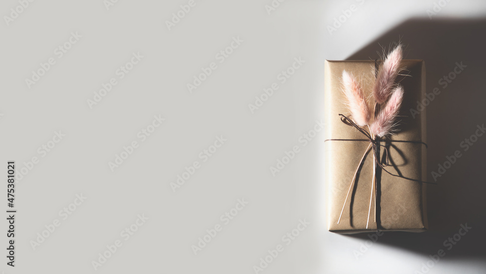 The gift box is decorated with dry pink flowers. Banner with a gift on a light background. Flat lay - obrazy, fototapety, plakaty 