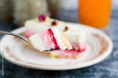 Appetizing slice of sweet mousse cake on a spoon close-up, brownie on a vintage plate, decorative christmas tree and glass of juice on a gray background.