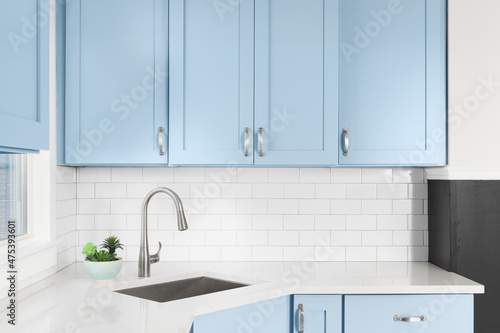 Detail of a kitchen with light blue cabinets  white granite countertop  subway tile backsplash  and a light hanging above a window.