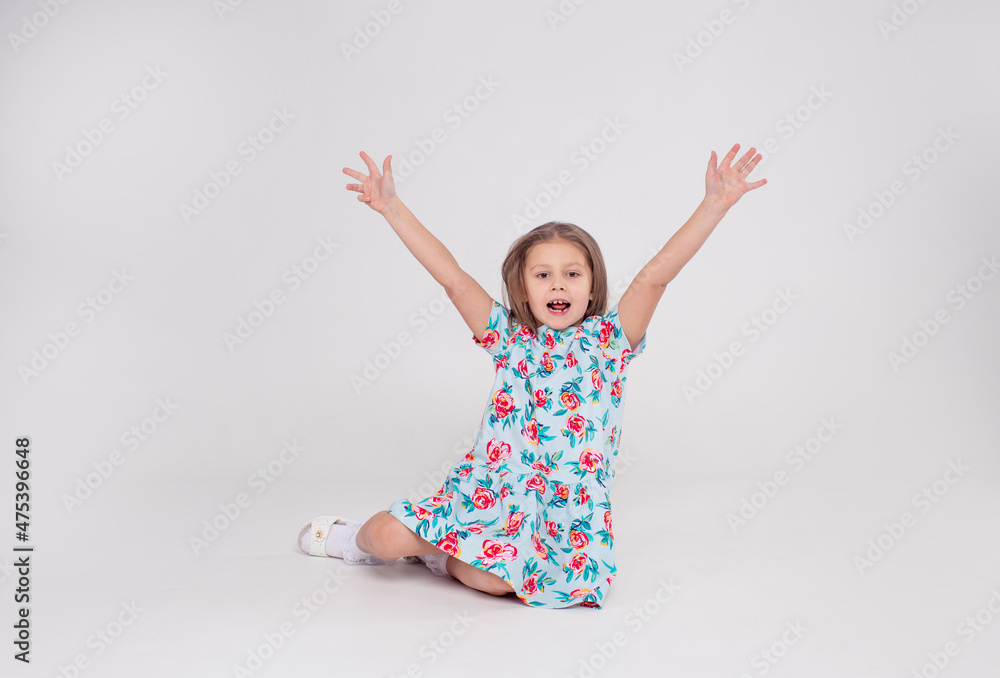 a beautiful little girl in a colorful bright dress laughs and raises her hands up sitting on a white isolated background a beautiful little girl in a colorful bright dress laughs and raises her hands up sitting on a white isolated background