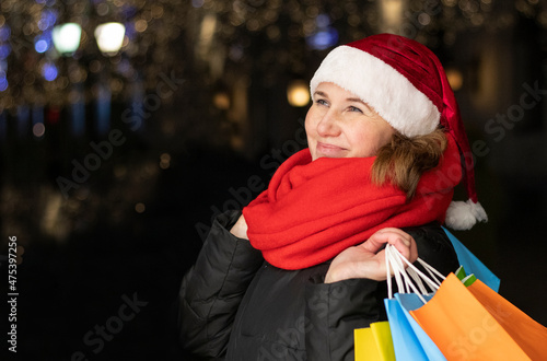 girl in a red santa claus hat with gifts in hands on the street of the city. Christmas mood