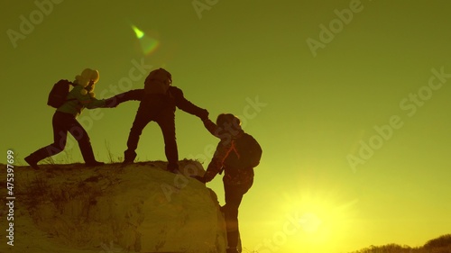 Silhouettes of climbers stretch out their hands to each other, climbing to the top of the hill. Travelers climb the cliff one by one. Teamwork of business people. A team of businessmen will win.