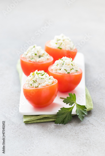 Fresh tomatoes stuffed with cottage ch eese and parsley on a serving tray on a linen napkinon a light gray background photo
