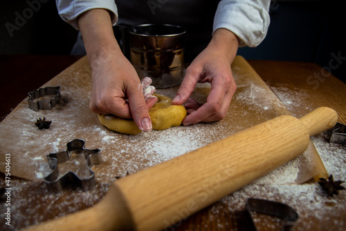 In the foreground is a table with baking parchment lying on it, on which there is dough that the cook's hands are crumpling, a rolling pin, baking molds and flour are scattered around. High quality