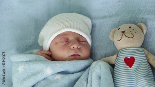 Close-up of Newborn Baby Face Portrait Early Days Sleeping With Tady Bear On Blue Background. Child At Start Minutes Of Life on Hat. Infants, Childbirth, First Moments Of Borning, Beginning Concept photo