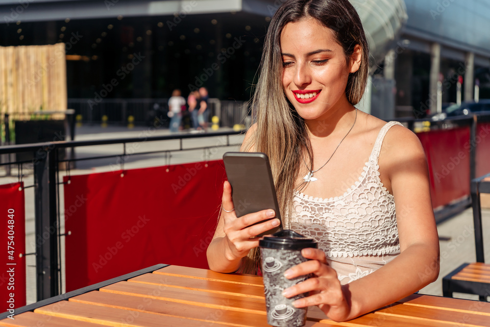 Medium shot of a beautiful woman sitting on the terrace of a bar having a drink while having a video conference on a sunny day. Space for text or copy space.