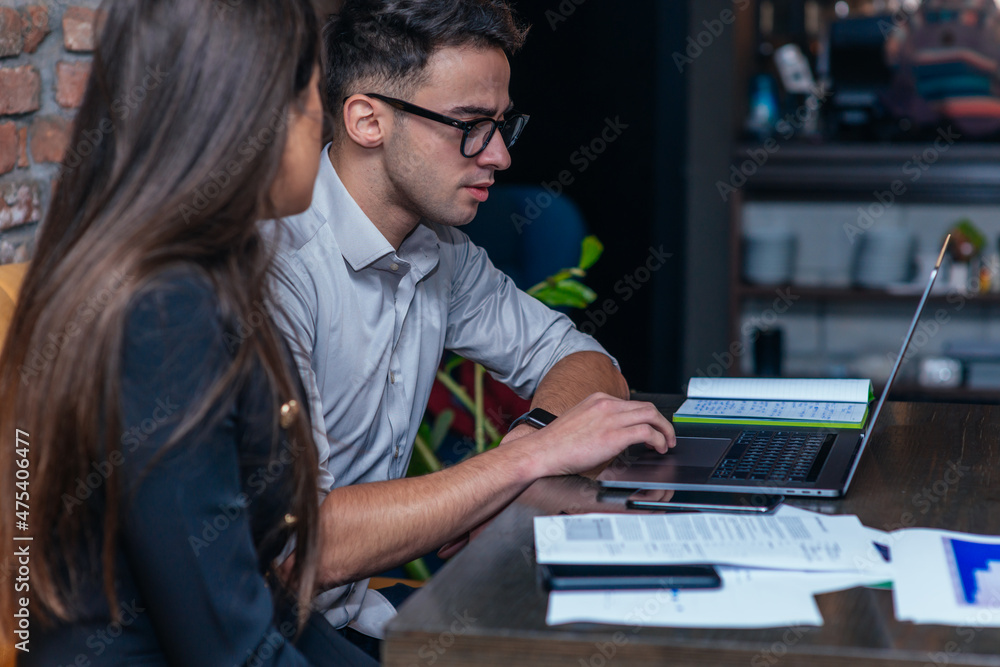 Business meeting inside a cafe with two young colleagues sitting at a table, sharing some new ideas and looking at their laptops