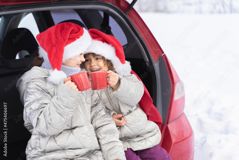 Merry Christmas. Happy Children holds a red mugs with hot tea in the trunk of the car In winter. Winter holidays. Christmas trips, family vacations