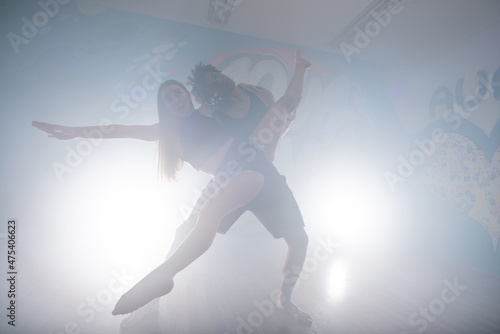 Group of multiracial dancers enjoying funky hip hop moves in dark studio with smoke and lighting. Group of young hip-hop dancers performing on the stage. Happy dancing women. © qunica.com