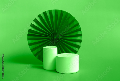 White cylindrical podium with red, green paper fan background for branding and product presentation. Chinese manets. Closeup. Monochrome photo