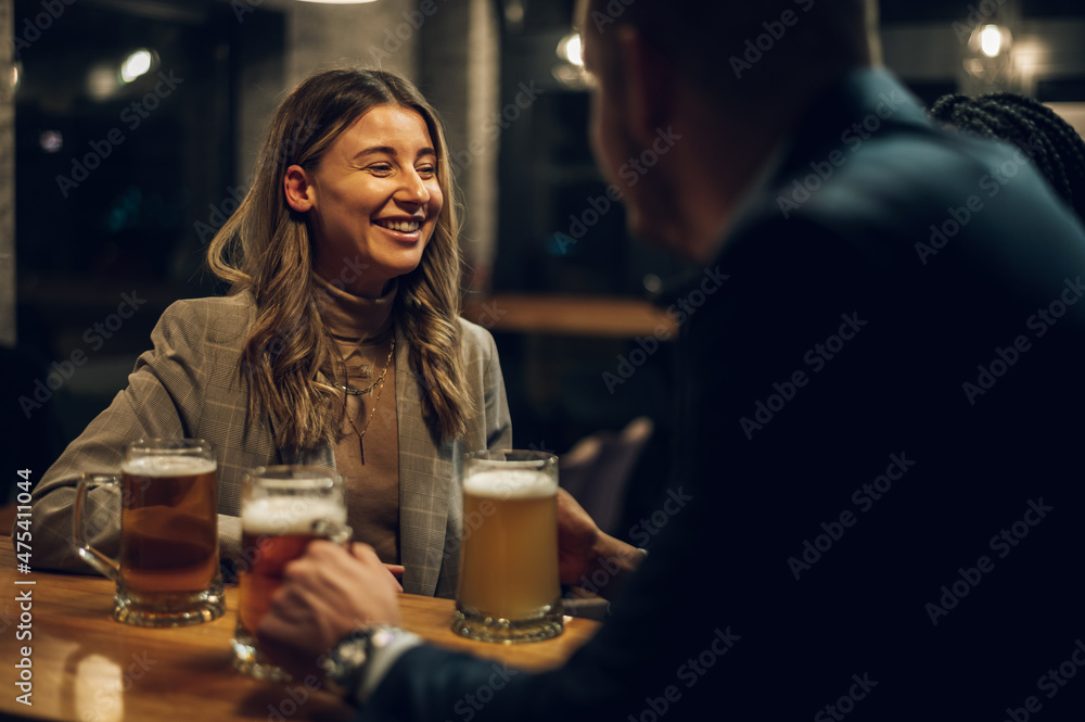 Cheerful colleagues drinking beer in the bar together after work and using a tablet