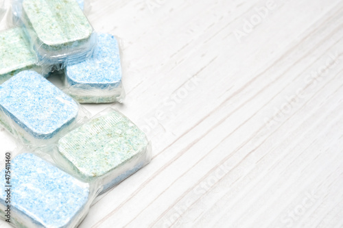 Green and blue dishwasher tablets in water-soluble packaging close up on the table with copy space