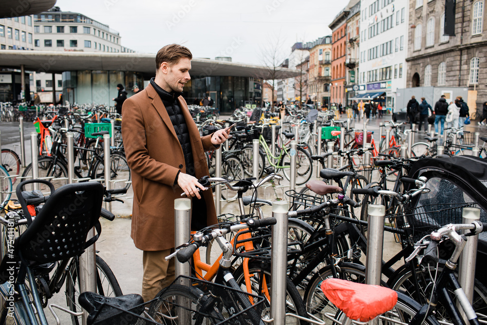 Young man unlocks bicycle with his mobile phone. Electric bicycle new way city mobility. Green transportation. Sustainable climate neutral cities goals. Ecology mobility sustainability transportation Young man unlocks bicycle with his mobile phone. Electric bicycle new way city mobility. Green transportation. Sustainable climate neutral cities goals. Ecology mobility sustainability transportation