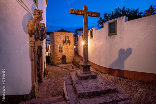 Europe, Portugal, Obidos. Church and cross on cobblestone street at sunset.