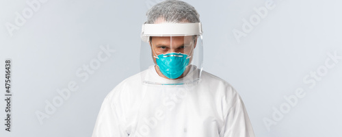 Covid-19, preventing virus, healthcare workers and vaccination concept. Close-up of determined serious doctor in personal protective equipment, medical respirator, working with dangerious diseases photo