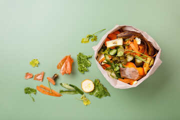 Sorted kitchen waste in paper eco bag on green background. Compost-container. Sustainable life style. Vegetable and fruit peels, scraps from food preparation collected in trash-pack for recycling