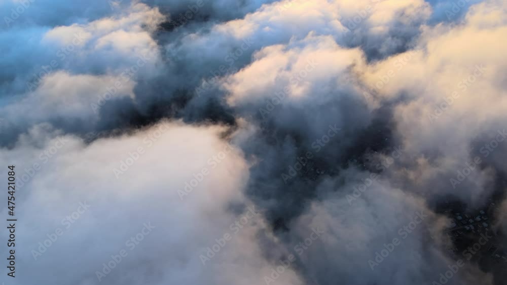 Aerial view from high altitude of distant city covered with puffy cumulus clouds flying by before rainstorm at sunset. Airplane point of view of landscape in cloudy weather Aerial view from high altitude of distant city covered with puffy cumulus clouds flying by before rainstorm at sunset. Airplane point of view of landscape in cloudy weather