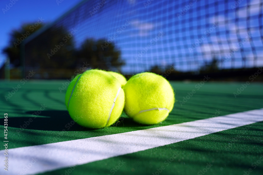 Tennis balls on tennis court with net in background.