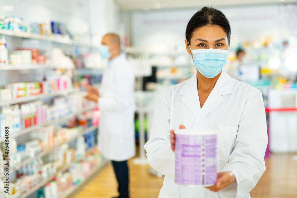 Female pharmacist in protective mask offers medicine while standing in the trading floor of a pharmacy