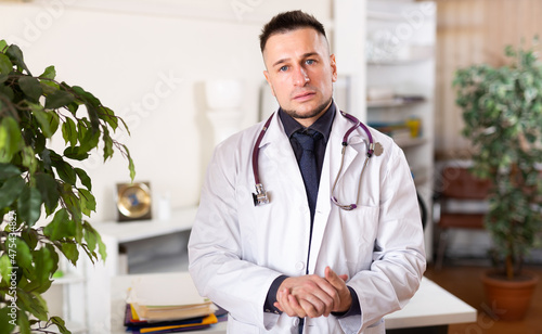 Portrait of friendly male doctor in white coat at clinic office photo