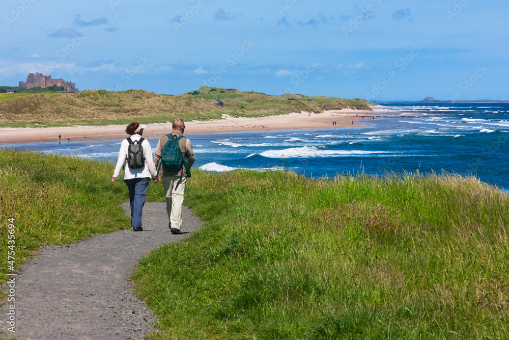 Tourists hiking along the coast of Northumberland, England, UK - obrazy, fototapety, plakaty 