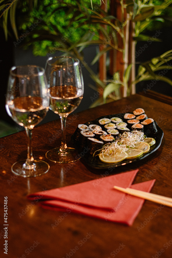 Sushi set na talerzu w restauracji z imbirem i wasabi, kieliszki wina, kolacja dla dwoch, obiad