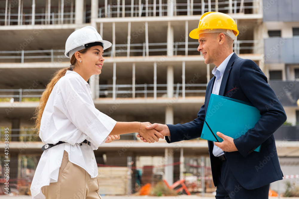 Portrait of two successful architects, friendly shaking hands, standing on a construction site
