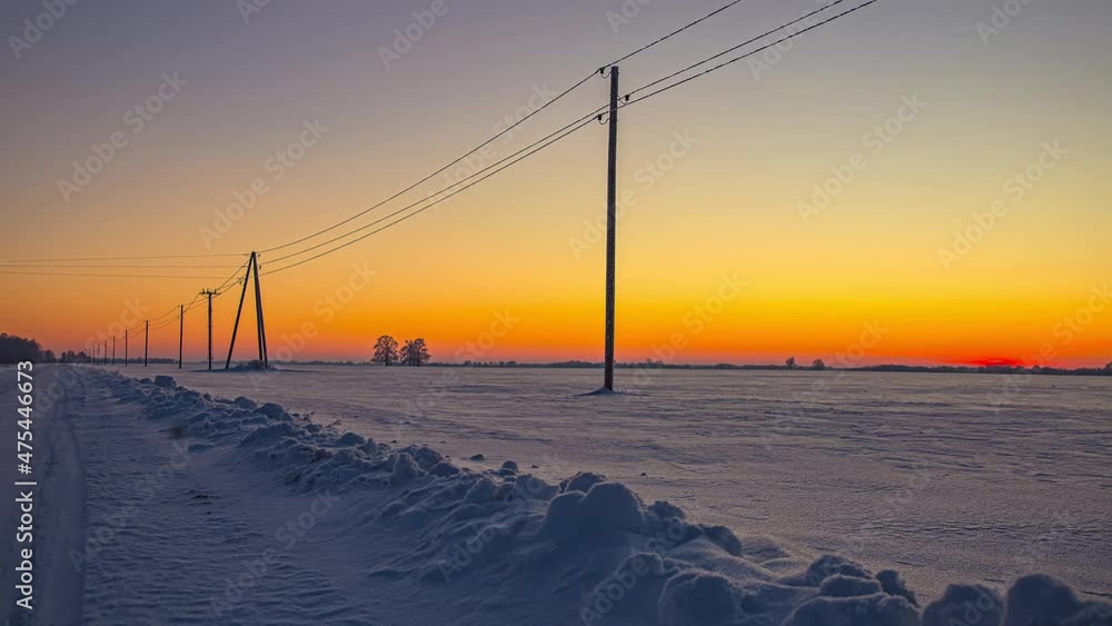 Time lapse shot of snowy winter field and orange and blue colored sky after sunset - Blue hour in rural landscape in the evening Time lapse shot of snowy winter field and orange and blue colored sky after sunset - Blue hour in rural landscape in the evening