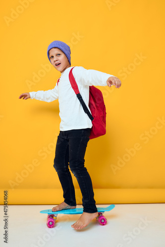 portrait of cute boys rides a skateboard in a blue hat yellow color background