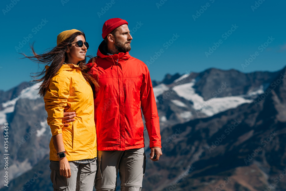 Portrait of travelers on the background of mountains. Portrait of travelers in tourist clothes in the mountains. A sporty couple on top of a mountain. An active couple is engaged in hiking. Copy space