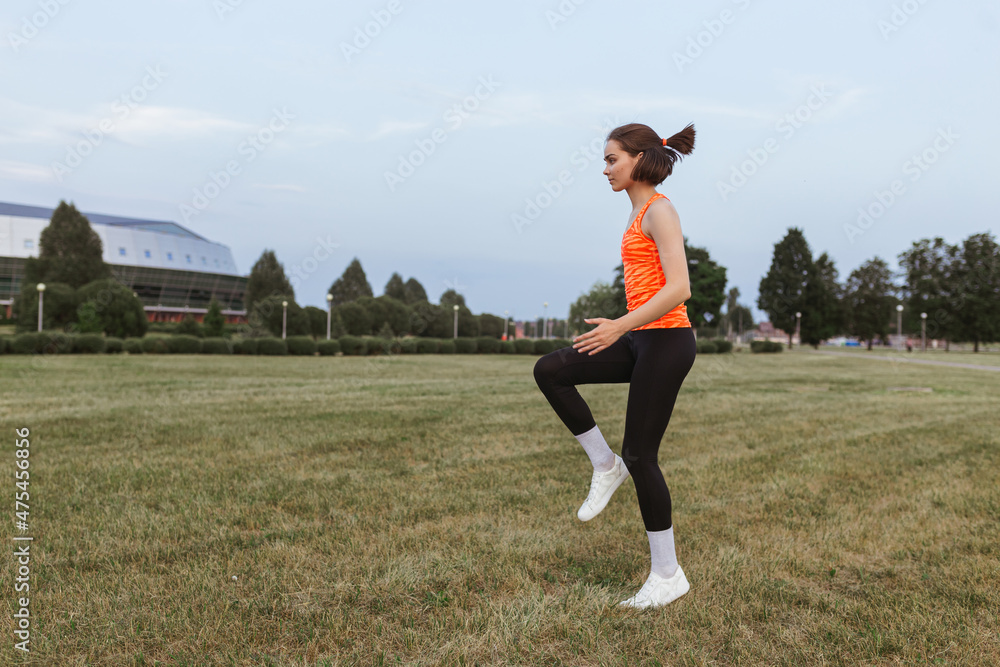 Side view of athletic sportswoman running in place and doing cardio training on meadow in summer 