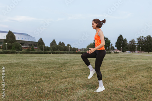 Side view of athletic sportswoman running in place and doing cardio training on meadow in summer 