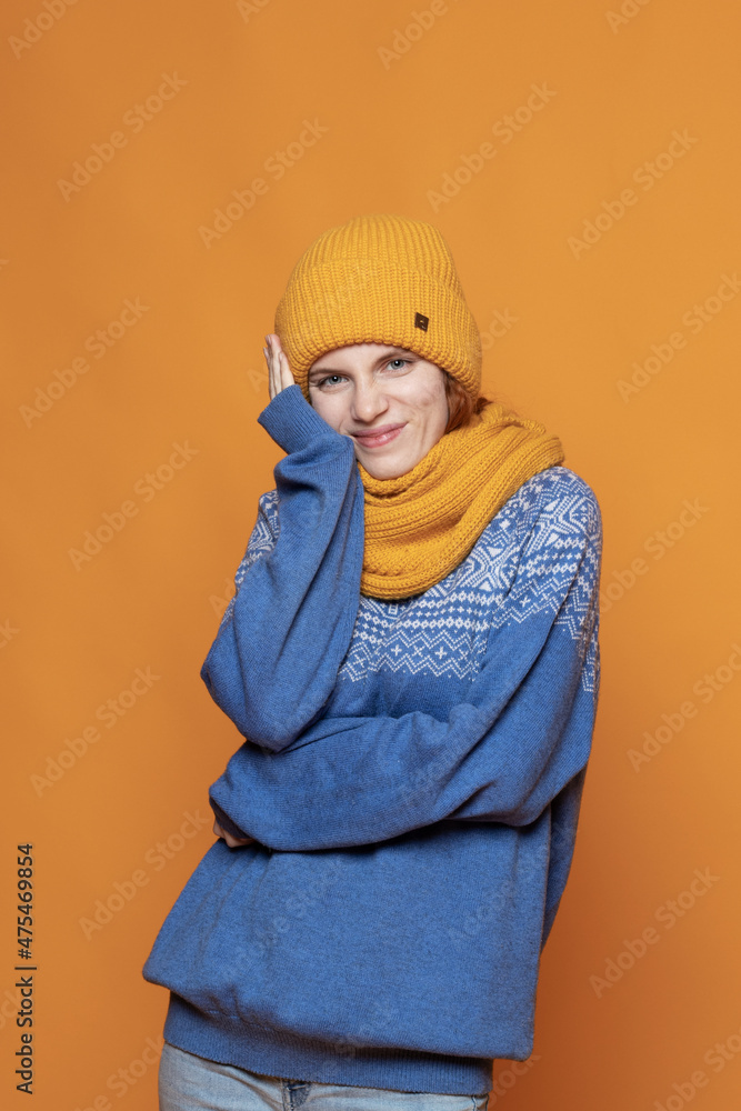 young red-haired girl in a warm hat and a knitted sweater on a yellow background young red-haired girl in a warm hat and a knitted sweater on a yellow background