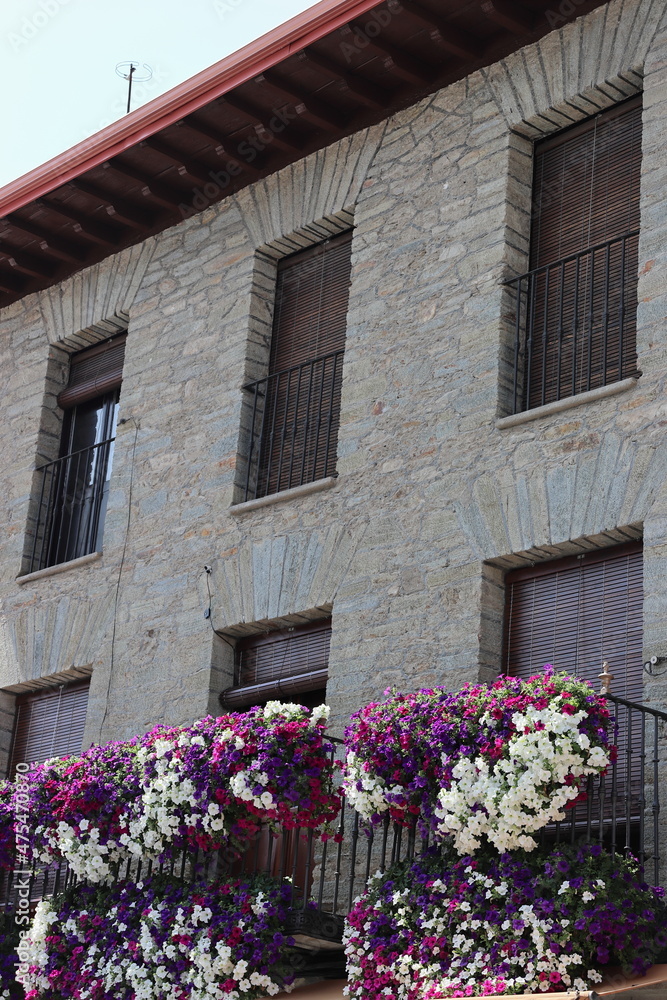 Close-up of a stone house with a railing, wooden blinds and geranium flowers decorating the balconies in Villafranca do Bierzo, León. Vertical image.