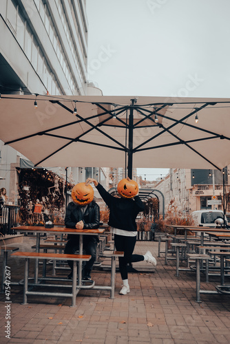 Guy and girl with pumpkin heads in a street cafe