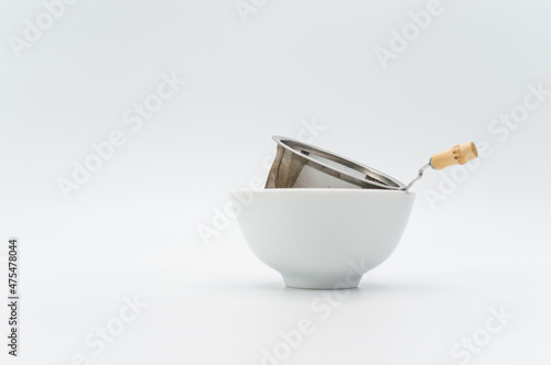 metal tea strainer in a white stoneware bowl on a white tabletop Fotobehang